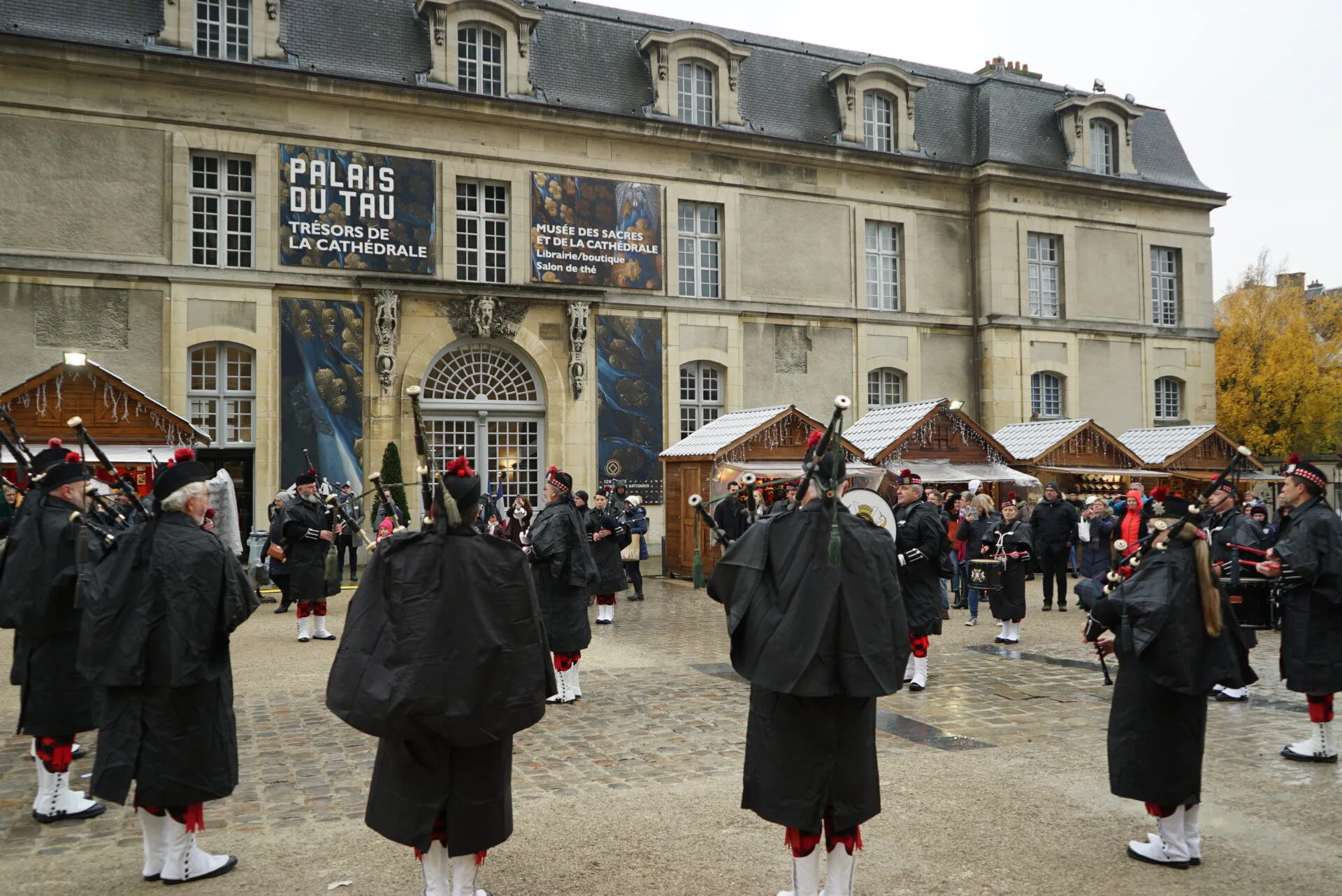 Des musiciens en kilt jouent devant le palais du Tau, entre des chalets du marché de Noël de Reims, en 2019