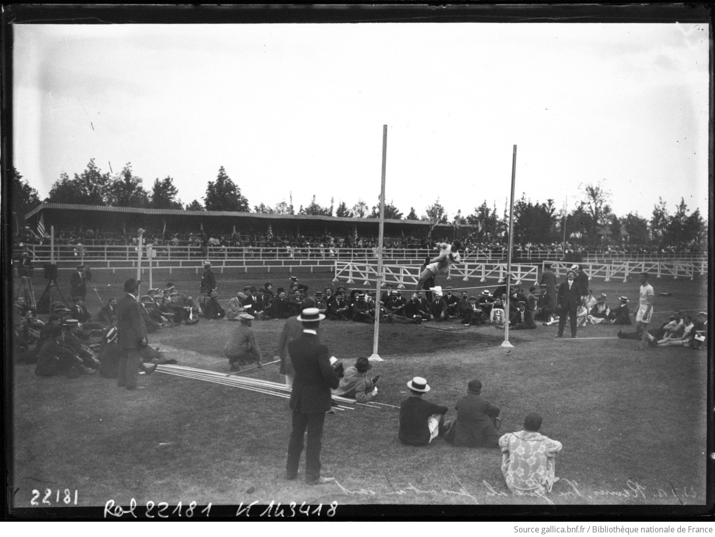 Un athlète franchit la barre lors d’un saut en hauteur devant des spectateurs assis au parc Pommery de Reims, en 1912
