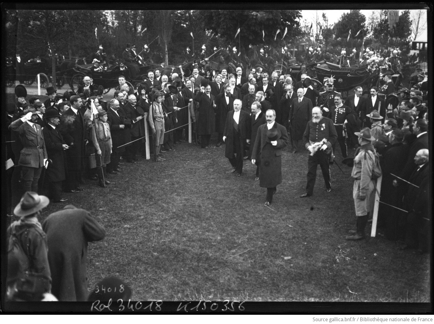 Le président Poincaré et des officiels marchent entre deux haies de spectateurs et de scouts au parc Pommery de Reims, en 1913