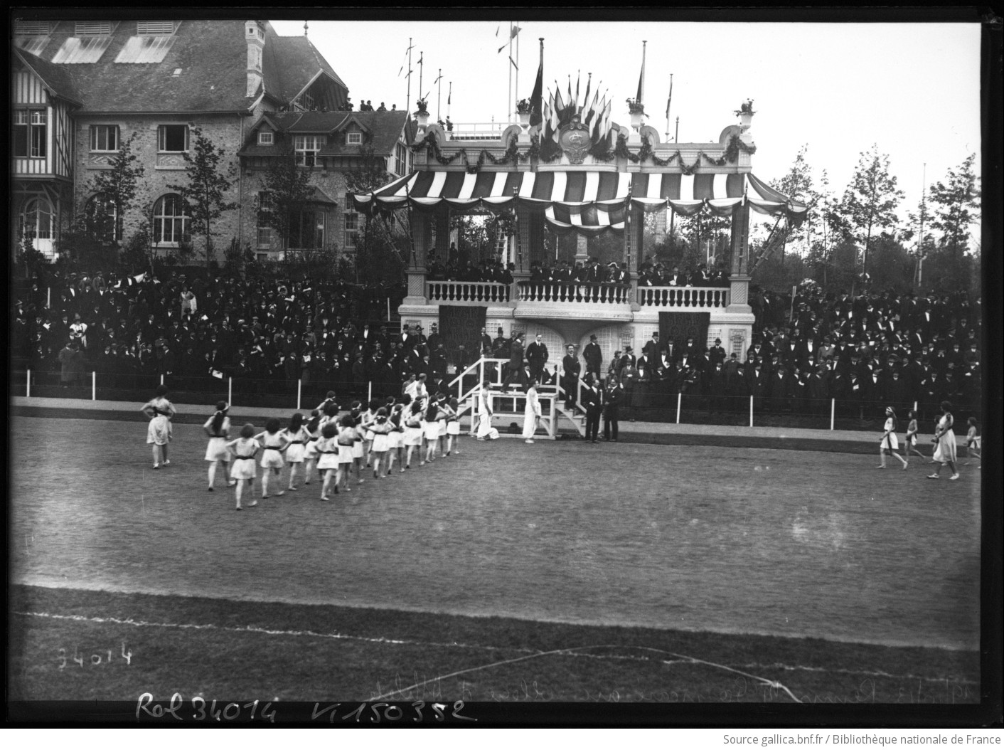Jeunes filles en gymnastique devant une tribune pavoisée et une foule au parc Pommery de Reims, en 1913